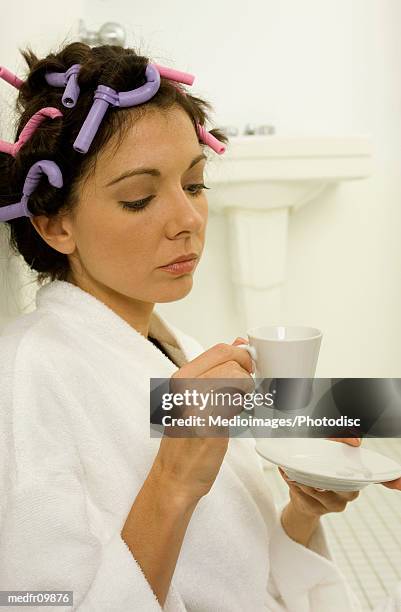 mid adult woman with curlers in her hair holding a cup and saucer - hair curlers stockfoto's en -beelden
