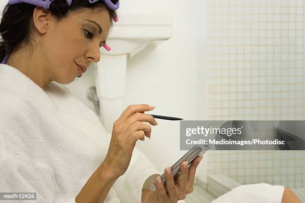 mid adult woman with curlers in hair using palmtop computer in bathroom, close-up, part of - hair curlers stockfoto's en -beelden