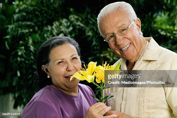 portrait of smiling senior couple holding yellow lilies outdoors, close-up - lili gentle fotografías e imágenes de stock