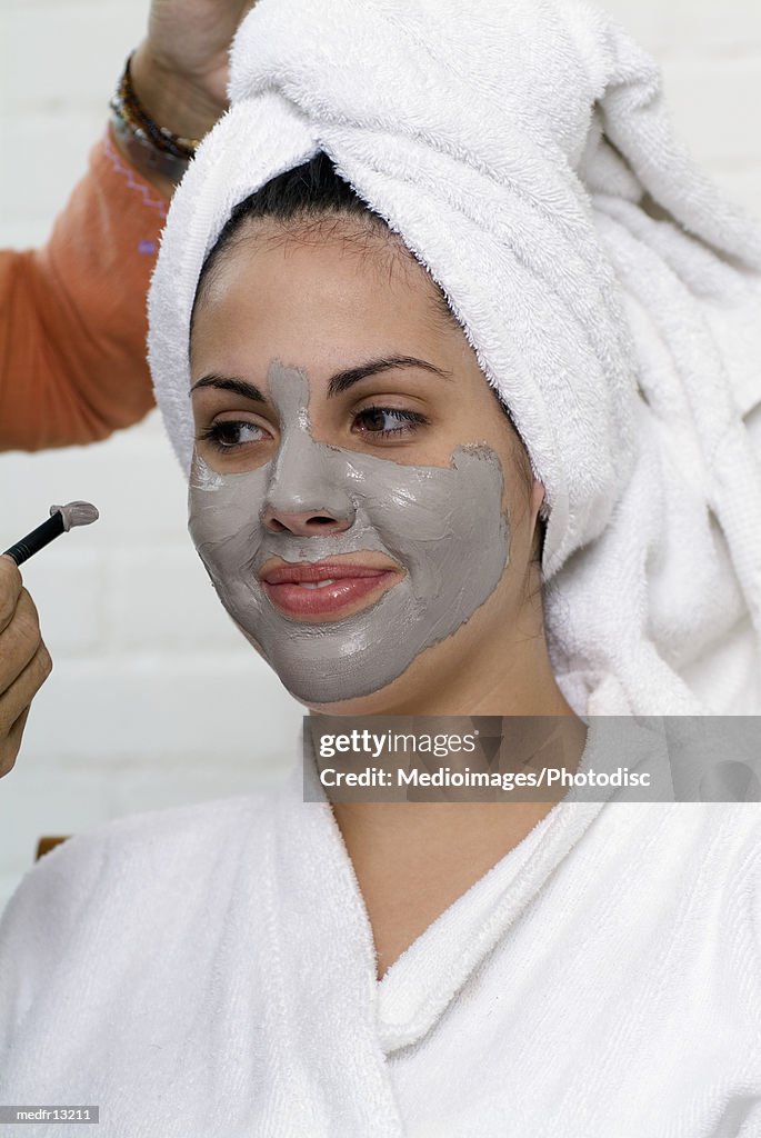 Smiling woman in robe with mud mask on face, close-up
