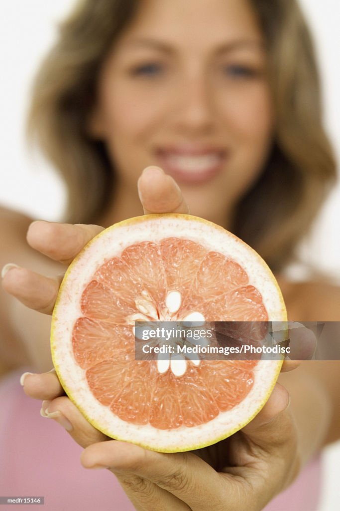 Smiling young woman holding out half of a grapefruit, close-up, selective focus, focus on grapefruit