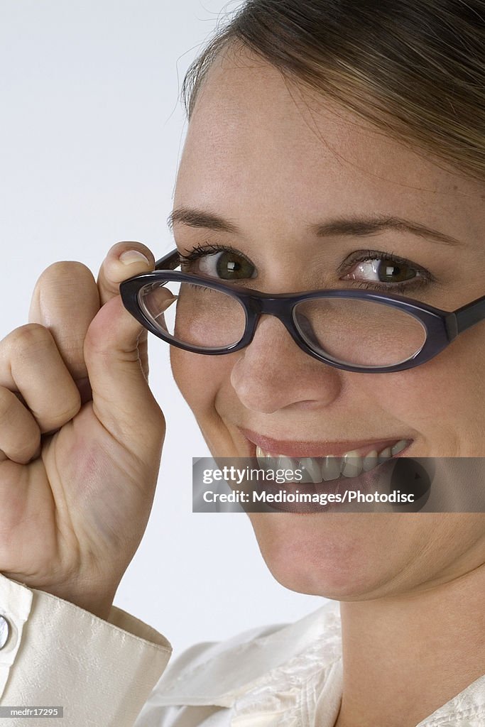 Smiling young businesswoman with hand on glasses, close-up