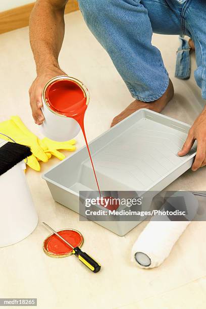 barefoot man pouring red paint into roller pan, close-up - pan stock-fotos und bilder