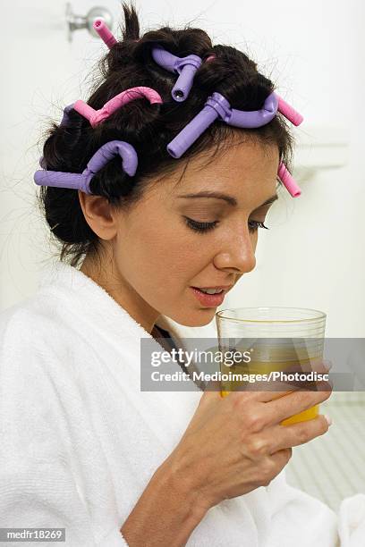 smiling mid adult woman with curlers in hair holding glass of orange juice, close-up - hair curlers stockfoto's en -beelden