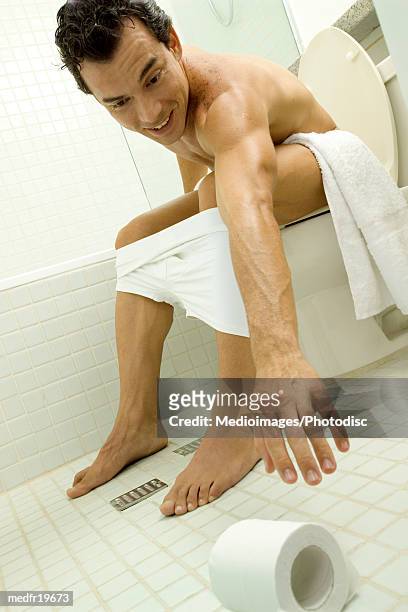 man sitting on a commode and reaching for toilet paper - commode stock pictures, royalty-free photos & images