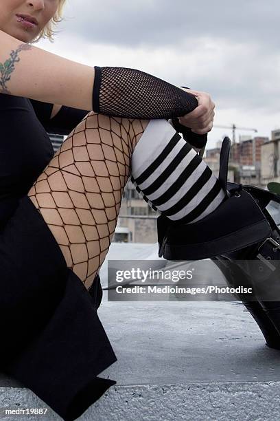 sad young goth woman with bleached hair sitting on roof - body modification stock-fotos und bilder