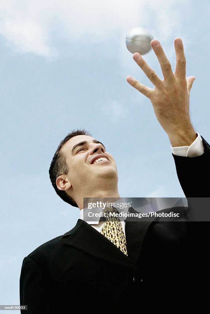 Businessman outdoors catching stress ball, low angle view, close-up