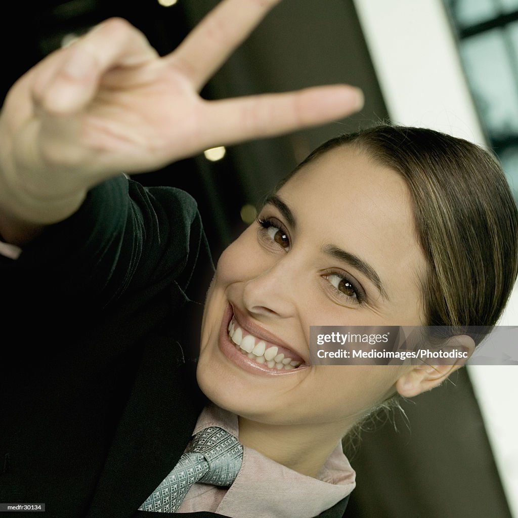 Smiling young businesswoman making V sign with fingers, close-up, tilt