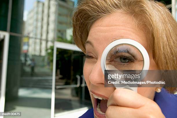mature businesswoman looking through a magnifying lens - looking through lens stock-fotos und bilder