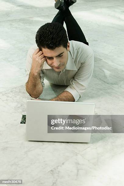 businessman resting head on hand and lying on floor working on laptop, overhead view - hand on head foto e immagini stock