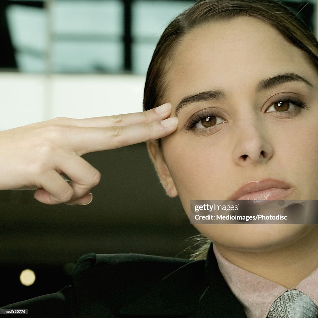 Serious young businesswoman holding two fingers against side of face, close-up