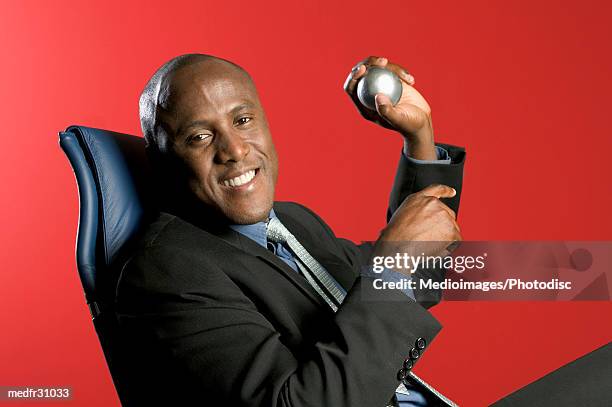 smiling black businessman sitting in chair and holding stress ball against red background, close-up - ball chair stock pictures, royalty-free photos & images