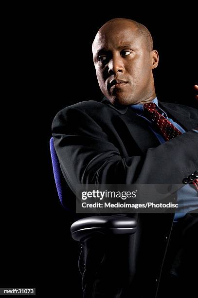 serious businessman sitting with arms crossed in office in high back chair - completo da uomo foto e immagini stock