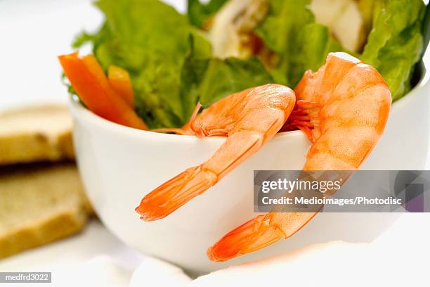 two shrimp with tails on hanging on the side of a bowl of salad, close-up, selective focus - oranje paprika stockfoto's en -beelden