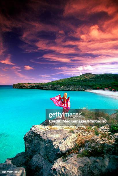 woman wearing a pareu and standing on the cliffs of knip beach, curacao, caribbean - curaçao fotografías e imágenes de stock