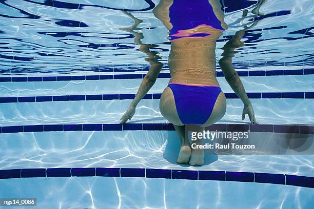 an underwater view of a bikini-clad woman kneeling on pool steps. - clad stockfoto's en -beelden