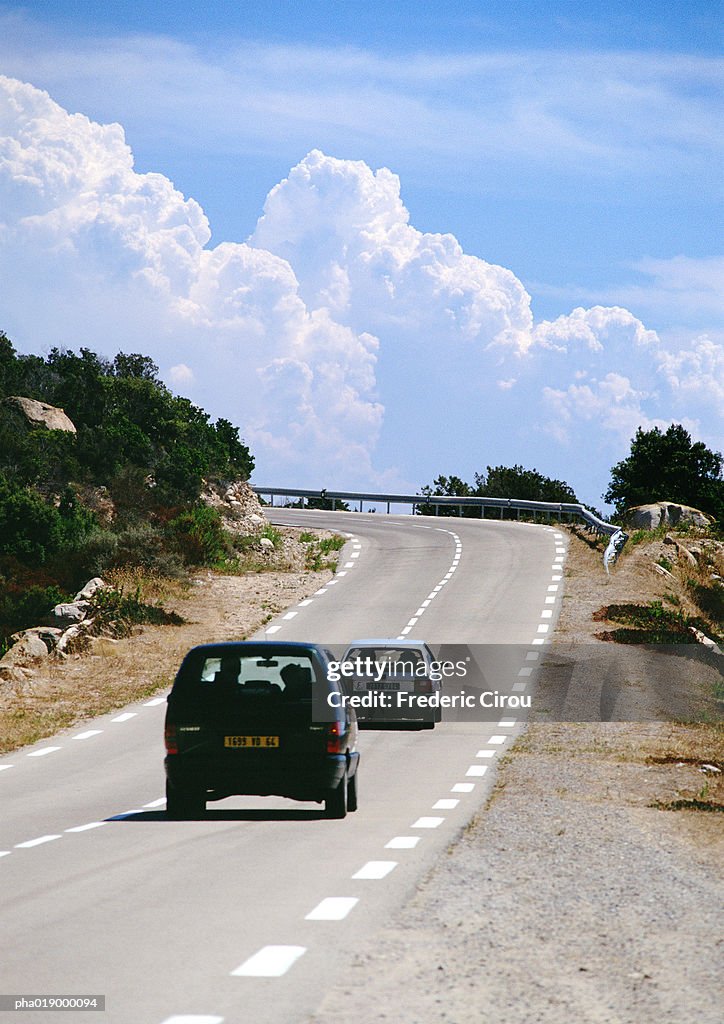 Cars on rural road, cloudscape in background