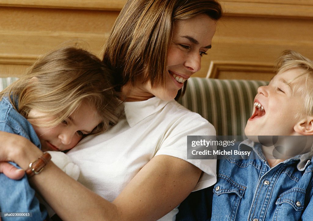 Woman holding girl in arms, looking at boy laughing