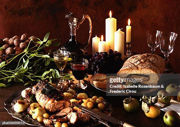 dishes of meats, fruits and vegetables, with carafe of wine and candles in background - festmahl stock-fotos und bilder