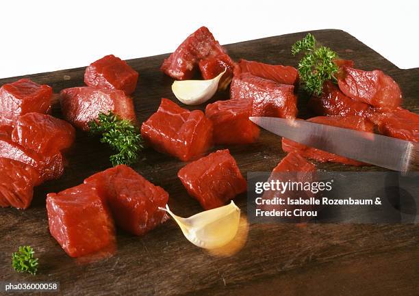 cubed beef on cutting board with knife, cloves of garlice and sprigs of parsley, close-up - beef bourguignon stock pictures, royalty-free photos & images