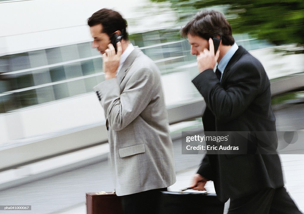 Two businessmen holding briefcase and cell phone, walking outside