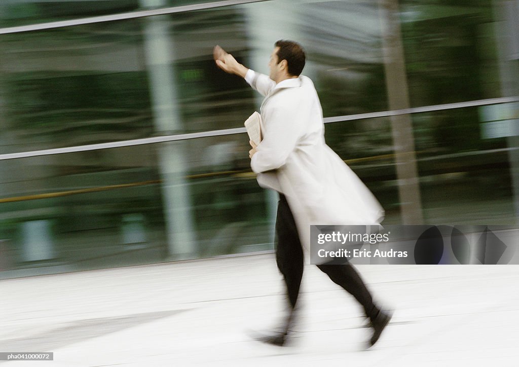 Businessman walking in street, hand raised, blurred