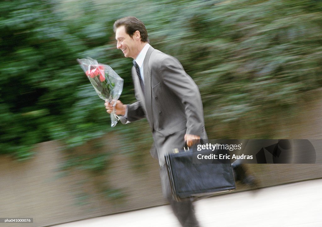 Businessman holding briefcase and bouquet of flowers, running, blurred