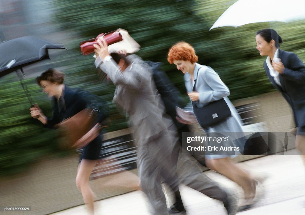 Businesspeople holding umbrella or briefcase above head, running, blurred