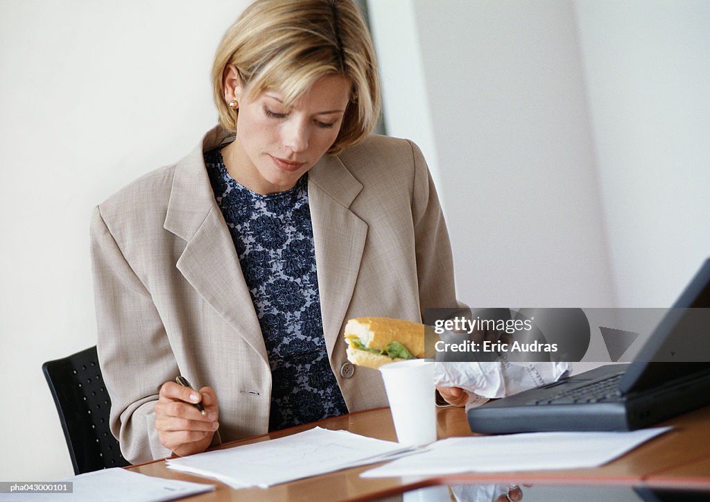 Businesswoman sitting at desk, holding sandwich