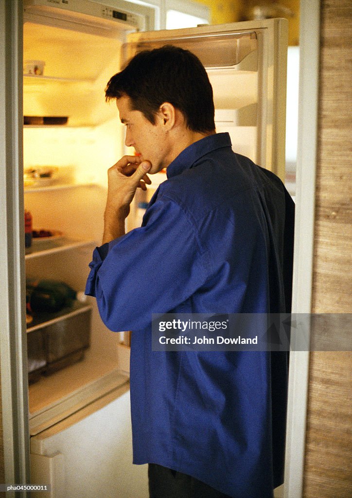 Man standing in front of open refrigerator, side view