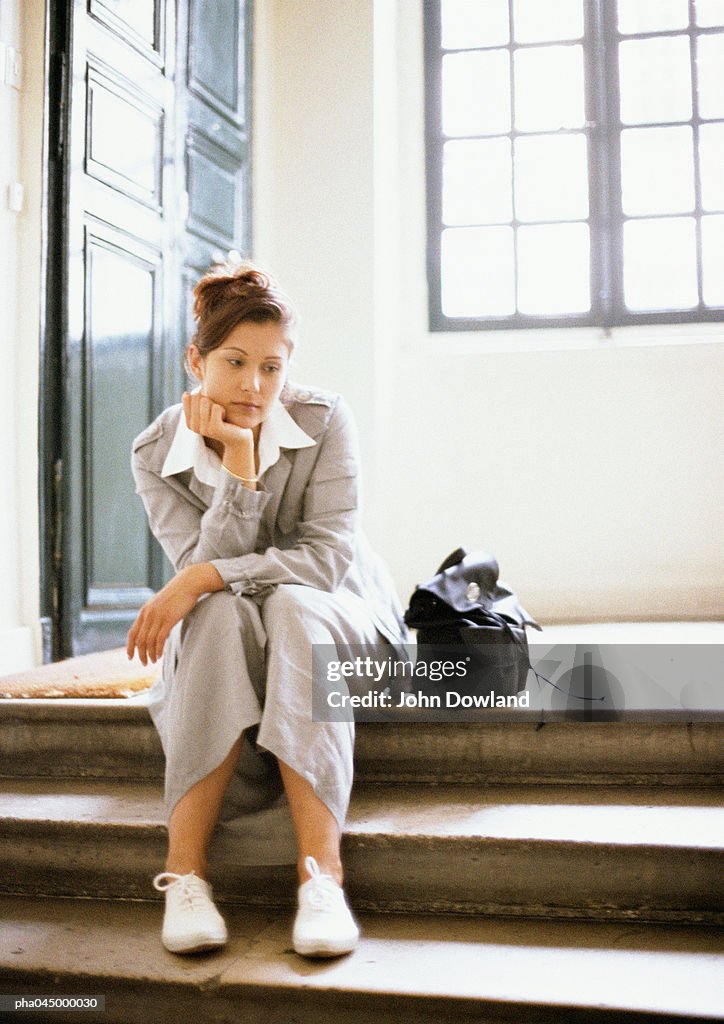 Woman sitting on steps, hand under chin, full length