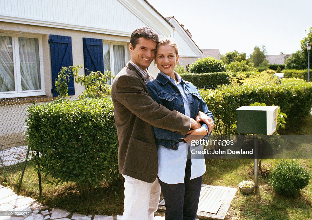 Couple standing in front of house, embracing