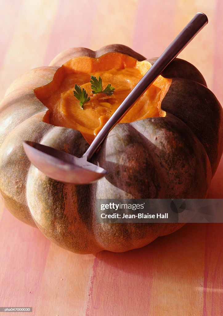 Pumpkin soup in pumpkin shell with ladle, close-up