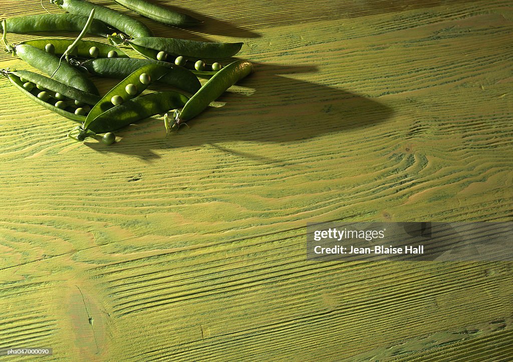 Peas in open pods on wood table, off centered
