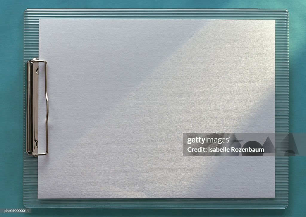 Clipboard holding blank white paper, horizontal, full length, close-up, teal background