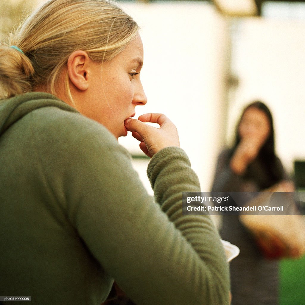 Profile of a female teenager in green, with her fingers in mouth