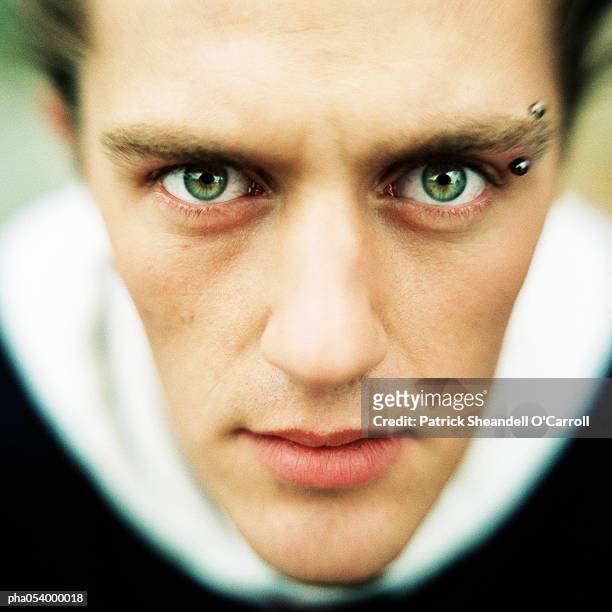 male teenager with an eyebrow piercing looking deeply into camera, close-up - body modification stock-fotos und bilder