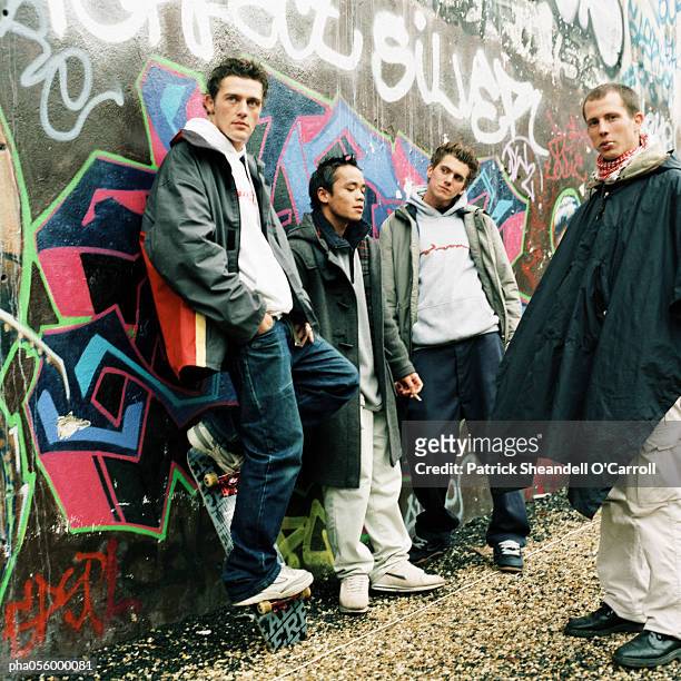 four young men in city street, three leaning back against graffiti wall - patrick wall stock pictures, royalty-free photos & images