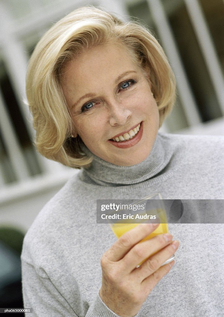 Woman looking at camera holding glass of orange juice, close up, portrait.