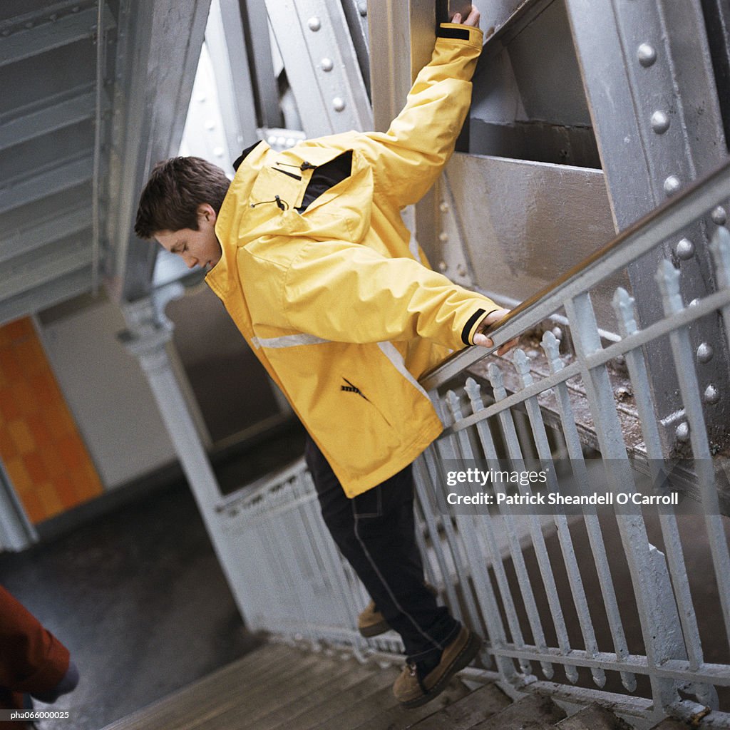 Man in raincoat sliding down handrail