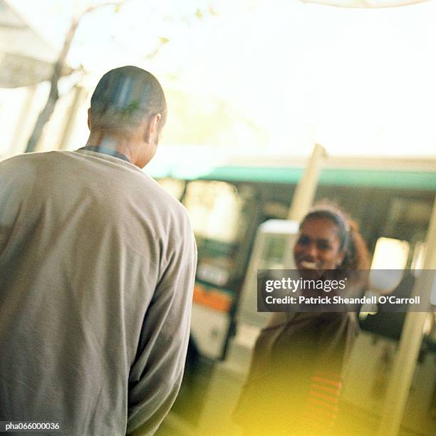 young man talking to young woman at bus station, outside. - africain stockfoto's en -beelden