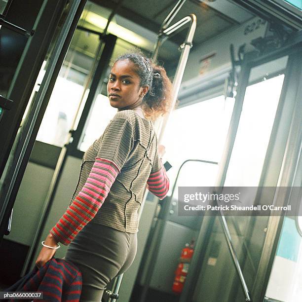 young woman holding rail, getting on bus, looking back over shoulder - africain stockfoto's en -beelden