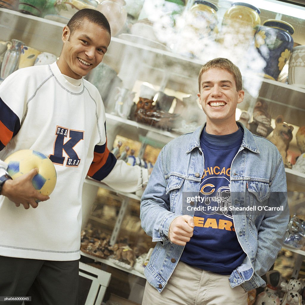 Young men leaning against store window, smiling, facing camera.