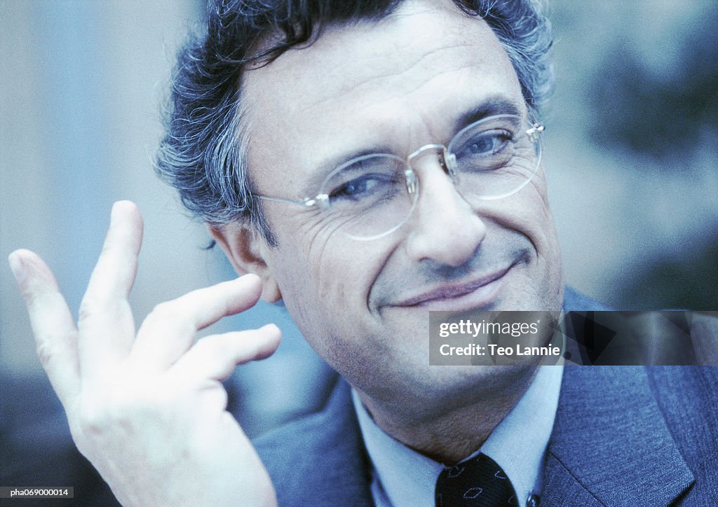 Man wearing suit and glasses, smiling, hand in air, close-up, cool toned.