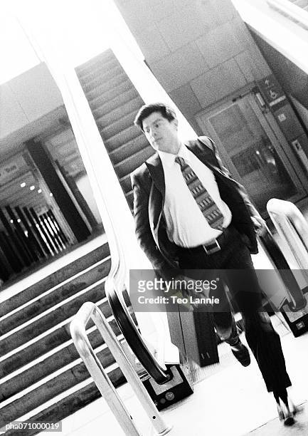 businessman getting off escalator, holding briefcase, blurred, b&w. - running up an escalator stock pictures, royalty-free photos & images
