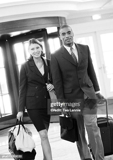 businessman and businesswoman walking together inside building with luggage, b&w. - africain stockfoto's en -beelden