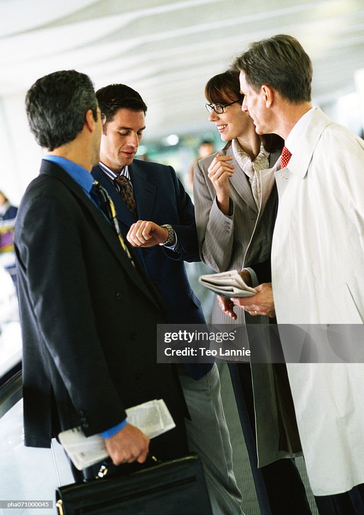 Business people standing together, one looking down at watch