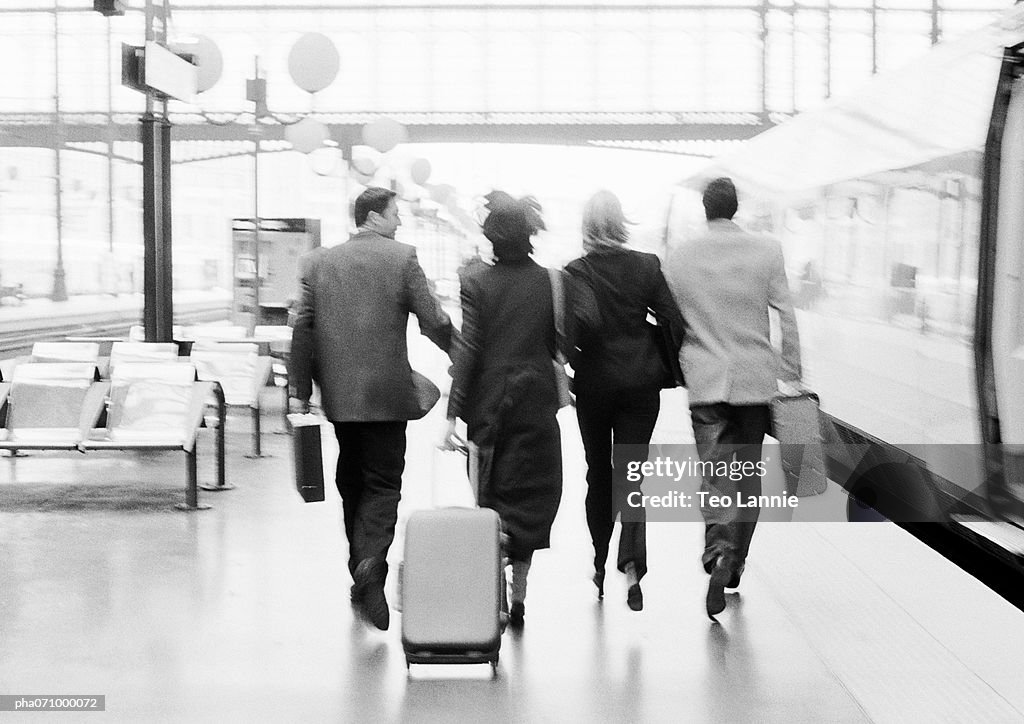 Group of business people walking next to train in station, rear view, b&w.