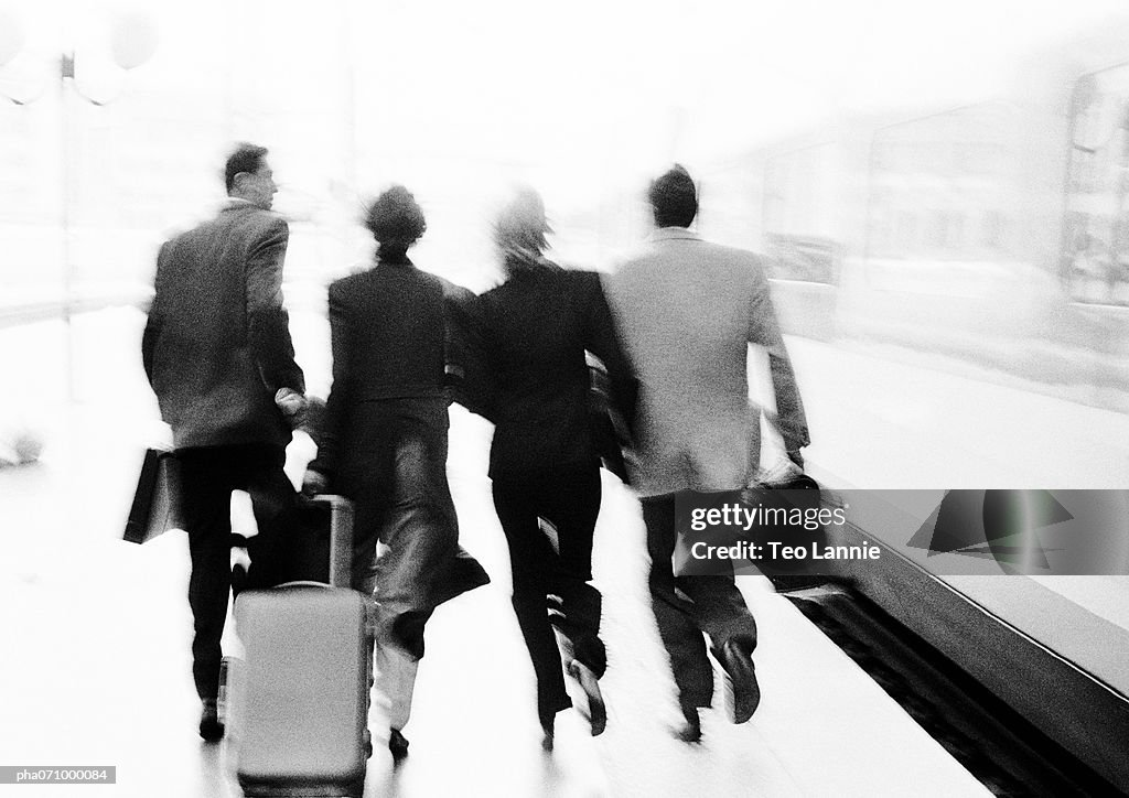 Group of business people walking near train, rear view, blurred, b&w.