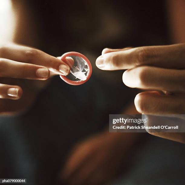 woman's fingers holding out condom toward man's fingers, close-up - condom stock pictures, royalty-free photos & images